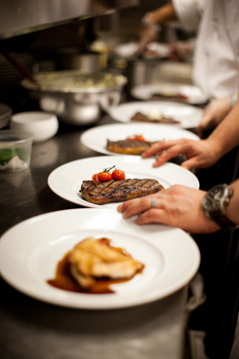 Platos recién emplatados, en fila sobre el pase, y las manos del cocinero