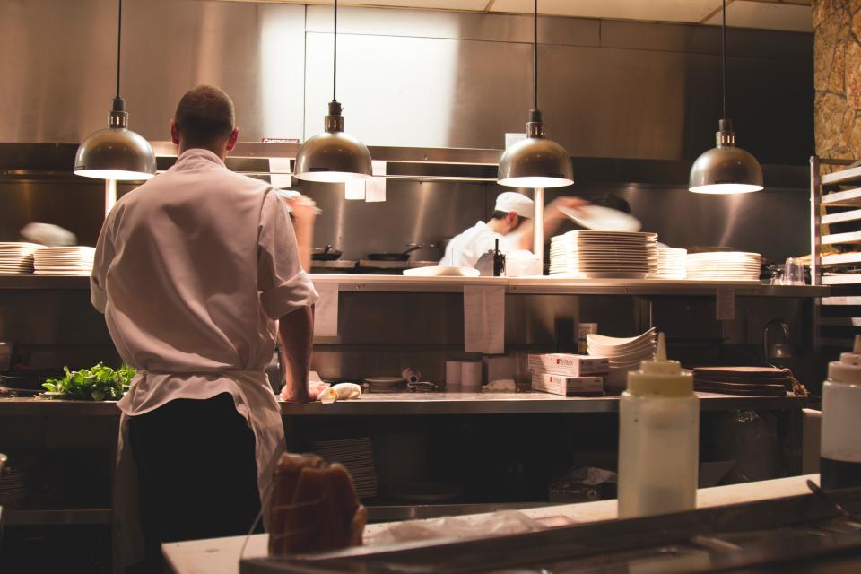 Una cocina de restaurante en pleno servicio, con las lámparas encendidas sobre el pase y los platos apilados